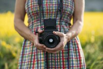 Femme en robe colorée tenant appareil photo dans la nature — Photo de stock