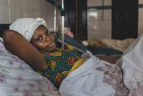 CAMEROON - AFRICA - APRIL 5, 2018: Adult ethnic woman lying on bed in hospital and looking at camera — Stock Photo