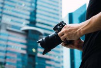 Gros plan des mains masculines tenant une caméra professionnelle debout dans la rue — Photo de stock