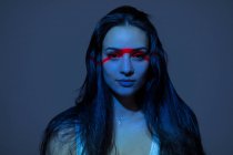 Молодая привлекательная женщина с красной линией на лице смотрит в камеру на темном фоне — стоковое фото