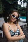 Retrato de jovem mulher asiática em óculos de sol em pé na piscina — Fotografia de Stock