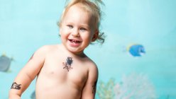 Cheerful cool toddler boy with instant tattoos smiling and looking at camera — Stock Photo