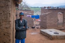 ANGOLA - ÁFRICA - 5 de abril de 2018 - Hombre negro mayor con los brazos cruzados de pie frente a la casa - foto de stock