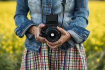 Mulher em vestido colorido e casaco de ganga segurando dispositivo de foto na natureza — Fotografia de Stock