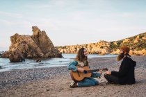 Mujer bonita sentada en la playa y tocando la guitarra para hombre - foto de stock