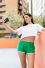 Молодая женщина в спортивной одежде стоя в городе улыбаясь и делая селфи со смартфоном — стоковое фото