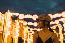 Modische junge Asiatin schaut abends in beleuchteter Stadt weg — Stockfoto