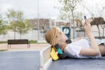 Menina loira deitada no chão com placa de centavo e usando smartphone — Fotografia de Stock