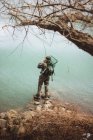 Pescatore in piedi con asta e bilanciamento su roccia al lago — Foto stock