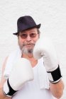 Дорослий чоловік в капелюсі і білі боксерські рукавички на грубій стіні . — стокове фото