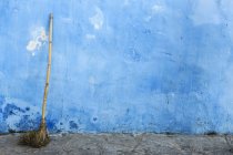 Старая метла перед синей плетеной стеной — стоковое фото
