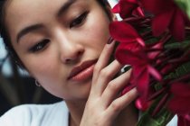 Досить молодий Азіатський жінка, стоячи і зворушливо червоні квіти — стокове фото