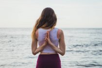 Woman standing and meditating with hands behind back at ocean — Stock Photo