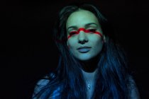 Giovane donna attraente con linea rossa sul viso guardando la fotocamera su sfondo nero — Foto stock