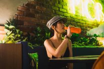 Élégante jeune femme asiatique assise dans un café et ayant une bouteille de boisson — Photo de stock