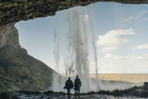 Back view of man and woman standing at the waterfall in hillside. — Stock Photo