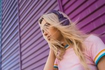 Mulher loira jovem com fones de ouvido roxos em pé na frente da parede colorida — Fotografia de Stock