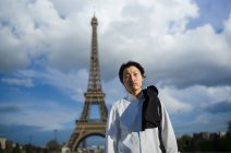 Pensativo chef japonés con uniforme de pie frente a la Torre Eiffel en París - foto de stock