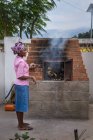 ANGOLA - AFRICA - APRIL 5, 2018 - African woman standing at furnace with smoking and burning wood fuel — Stock Photo