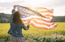 Mulher de saia colorida segurando bandeira americana no campo com flores amarelas no Dia da Independência — Fotografia de Stock