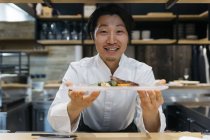 Chef sorridente che mostra piatto di cibo nel ristorante — Foto stock