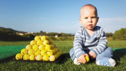 Entzückender kleiner Junge sitzt auf grünem Rasen an einem Haufen gelber Golfbälle — Stockfoto