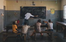 CAMERÚN - ÁFRICA - 5 DE ABRIL DE 2018: Niños africanos sentados en clase mientras el maestro limpia la pizarra - foto de stock