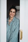 Fröhliche junge Frau im Schlafanzug, die vor der Tür steht und in die Kamera schaut — Stockfoto