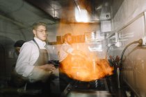 Cuoco facendo un flambe in cucina ristorante con i colleghi sullo sfondo — Foto stock