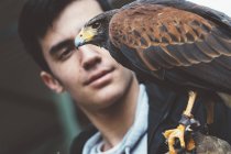 Jovem de pé e olhando para o falcão sentado na mão no zoológico — Fotografia de Stock