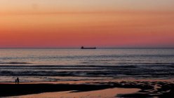 Яскравий вид на людей на береговій лінії в вечірній час з барвистим небом заходу сонця і вітрильним човном далеко на горизонті — стокове фото