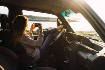 Женщина фотографируется со смартфоном в машине на природе — стоковое фото