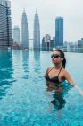 Азиатка отдыхает в бассейне с небоскребами на заднем плане — стоковое фото