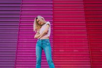 Selbstbewusste blonde Frau mit verschränkten Armen steht vor heller, bunter Wand — Stockfoto