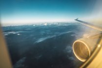 Shot through glass of plane glass with aircraft wing and turbine flying above blue cloudy sky — Stock Photo