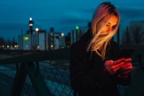 Donna bionda che utilizza lo smartphone sulla strada al tramonto — Foto stock