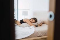 Donna sensuale con tatuaggi che indossano biancheria intima di pizzo nero sdraiato sul letto — Foto stock