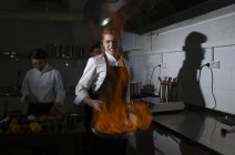 Приготовление фламбе на кухне ресторана с коллегами на заднем плане — стоковое фото