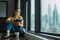 Frau mit Tasse sitzt auf dem Boden am Fenster und macht sich Notizen — Stockfoto