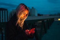 Блондинка використовує смартфон на вулиці в сутінках — стокове фото