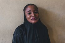 Камерун - Африка - 5 квітня 2018: Веселий африканською жінкою в чорний одяг, стоячи біля стіни і дивлячись на камеру — стокове фото