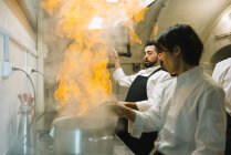 Cook making a flambe in restaurant kitchen with colleague watching — Stock Photo