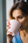 Primer plano de la mujer rubia pensativa bebiendo café de la taza rosa y mirando hacia otro lado - foto de stock