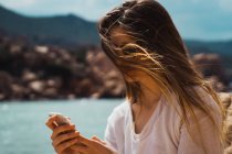 Frau mit langen braunen Haaren nutzt Smartphone am Meer — Stockfoto