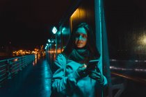 Young woman using smartphone and walking on street at night — Stock Photo