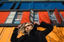 Mulher loira atraente olhando para longe contra edifício colorido — Fotografia de Stock