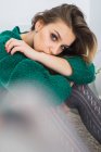 Красивая девушка в зеленом свитере сидит и смотрит в камеру — стоковое фото