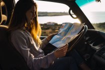 Junge Frau sitzt und liest Landkarte im Auto in der Natur — Stockfoto
