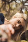 Молода блондинка спирається на дерево і дивиться на камеру — стокове фото