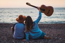 Homem e mulher sentados com guitarra na praia à beira-mar — Fotografia de Stock